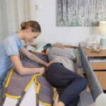 Bild på en säng och en vårdare hjälper vårdtagare att vända sig