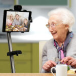 Äldre kvinna som äter middag. Hon har samtidigt bildsamtal med sin familj och även de äter.