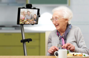 Äldre kvinna som äter middag. Hon har samtidigt bildsamtal med sin familj och även de äter.